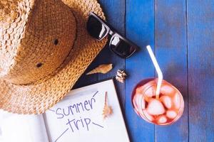 hoed met zonnebril, rood cocktail, kalender en schelpen Aan blauw geschilderd hout plank achtergrond. zomer vakantie concept foto