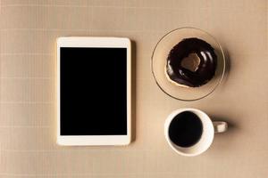 top visie van tablet met koffie kop en donut Aan tafel. foto