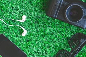 camera met zonnebril, slim telefoon en oortelefoons Aan groen gras achtergrond. foto