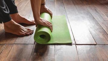 detailopname van een Mens met de hand rollen een groen yoga mat of oefening mat na oefenen ochtend- welzijn yoga praktijk Bij huis. gezond leven en gezond leven concept. foto