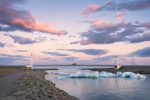 mooi zonsondergang over- suspensie brug Aan jokulsarlon glaciaal rivier- lagune met ijsberg drijvend in zuidelijk van vatnajokull nationaal park Bij IJsland foto