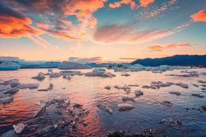 zonsondergang over- ijsberg en ijs breken drijvend in jokulsarlon gletsjer lagune, vatnajokull nationaal park, IJsland foto