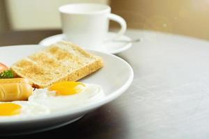 Amerikaans ontbijt en warme koffie in een witte keramische koffiekop op een houten tafel met warme ochtendzon en lens flare achtergrond. foto