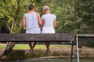 paar genieten van watermeloen terwijl zittend Aan de houten brug foto