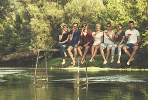 vrienden genieten van watermeloen terwijl zittend Aan de houten brug foto