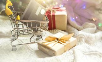 doos met een geschenk in Kerstmis verpakking in boodschappen doen kar Aan wit gebreid deken. zwart vrijdag, buying cadeaus voor nieuw jaar. vakantie decor, bank plastic kaart - zonder contant geld betaling, online op te slaan. kopiëren ruimte foto