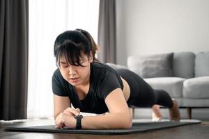 Aziatische mollige jonge vrouw die plankoefening doet en thuis naar het smartwatch-scherm kijkt. foto