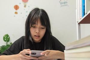 Aziatisch jong meisje gebruik een mobiel slim telefoon naar studie onderwijs online Bij huis. foto