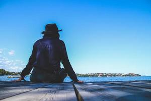 een vrouw eenzaam zittend Aan de houten pier Bij de zee met blauw lucht. foto