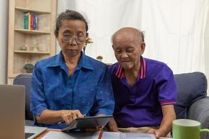 Aziatisch ouderen zitten en Holding rekenmachine voor verzekering of medisch onkosten en een computer Aan bureau huis. foto