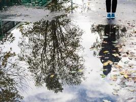 tiener in de buurt regen plas met Aan boom reflectie foto