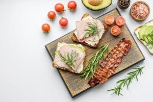 vers, heerlijk ham, boter, avocado en sesam zaden boterhammen Aan een houten snijdend bord foto