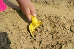 iemand gebruik een geel Schep kinderen speelgoed- lepel zand Aan de strand. foto
