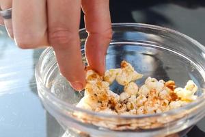 vrouw hand- nemen popcorn uit van een glas schaal. foto