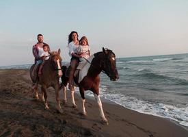 de familie besteedt tijd met hun kinderen terwijl rijden paarden samen Aan een mooi zanderig strand Aan zonsondergang. foto