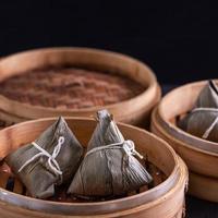 rijst knoedel, zongzi - drakenboot festival, stelletje traditioneel Chinees gekookt voedsel in stoomboot op houten tafel op zwarte achtergrond, close-up, kopieer ruimte foto