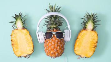 grappige ananas met witte hoofdtelefoon, concept van het luisteren van muziek, geïsoleerd op een gekleurde achtergrond met tropische palmbladeren, bovenaanzicht, plat ontwerp. foto