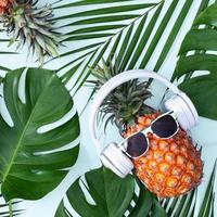 grappig ananas vervelend wit koptelefoon, concept van luisteren muziek, geïsoleerd Aan blauw achtergrond met tropisch palm bladeren, top visie, vlak leggen ontwerp.