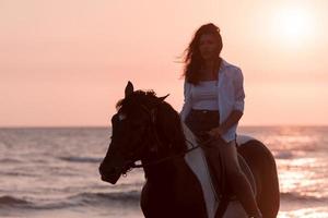 vrouw in zomer kleren geniet rijden een paard Aan een mooi zanderig strand Bij zonsondergang. selectief focus foto