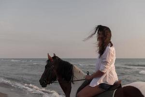 vrouw in zomer kleren geniet rijden een paard Aan een mooi zanderig strand Bij zonsondergang. selectief focus foto