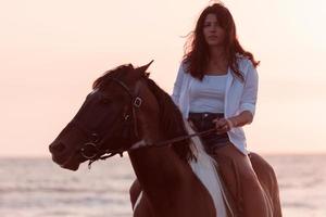 vrouw in zomer kleren geniet rijden een paard Aan een mooi zanderig strand Bij zonsondergang. selectief focus foto