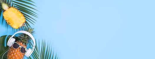 grappige ananas met witte hoofdtelefoon, concept van het luisteren van muziek, geïsoleerd op een gekleurde achtergrond met tropische palmbladeren, bovenaanzicht, plat ontwerp. foto