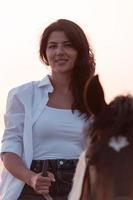 vrouw in zomer kleren geniet rijden een paard Aan een mooi zanderig strand Bij zonsondergang. selectief focus foto