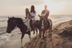 de familie besteedt tijd met hun kinderen terwijl rijden paarden samen Aan een mooi zanderig strand Aan zonsondergang. foto