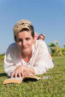 vrouw aan het liegen en lezing haar favoriete boek Aan een weide gedekt met vers groen gras Aan een zonnig zomer of voorjaar dag. foto