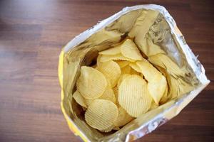 Aardappelchips in open snackzak close-up op tafelvloer foto