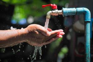 waterconcept in het dagelijks leven. handen ondersteunen het water dat uit de kraan stroomt. water dat uit de kraan spat foto