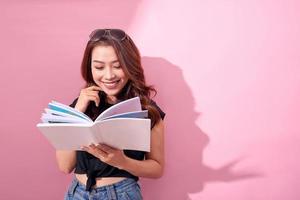 beeld van glimlachen jong vrouw poseren geïsoleerd over- roze achtergrond muur Holding boek lezing. foto