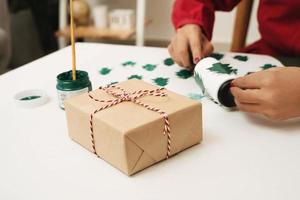 dichtbij omhoog van vrouw handen maken geschenk papier Hoes voor Kerstmis. Kerstmis concept. foto