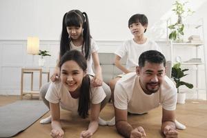 gelukkig welzijn aziatische thaise familie, kinderen spelen en plagen hun ouders terwijl yoga-fitnesstraining en gezondheidsoefening samen in de witte woonkamer, huiselijke thuislevensstijl, weekendactiviteit. foto