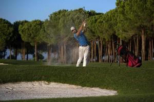 golfspeler raken een zand bunker schot Aan zonsondergang foto