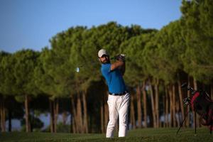 golfspeler raken een zand bunker schot Aan zonsondergang foto