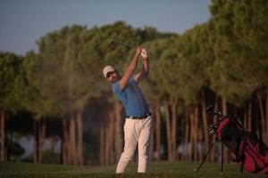 golfspeler raken een zand bunker schot Aan zonsondergang foto