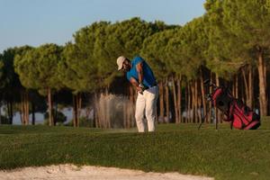 golfspeler raken een zand bunker schot Aan zonsondergang foto