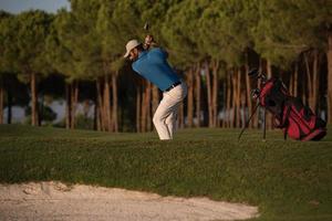 golfspeler raken een zand bunker schot Aan zonsondergang foto