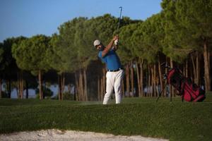 golfspeler raken een zand bunker schot Aan zonsondergang foto