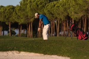 golfspeler raken een zand bunker schot Aan zonsondergang foto