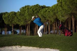 golfspeler raken een zand bunker schot Aan zonsondergang foto