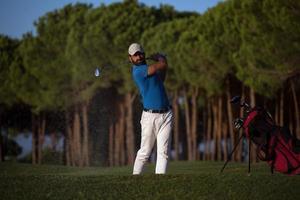 golfspeler raken een zand bunker schot Aan zonsondergang foto