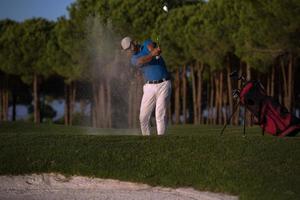 golfspeler raken een zand bunker schot Aan zonsondergang foto