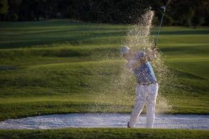 golfspeler raken een zand bunker schot Aan zonsondergang foto