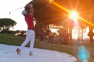 golfspeler raken een zand bunker schot Aan zonsondergang foto