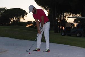 golfspeler raken een zand bunker schot Aan zonsondergang foto