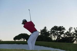 golfspeler raken een zand bunker schot Aan zonsondergang foto