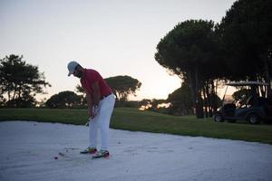 golfspeler raken een zand bunker schot Aan zonsondergang foto