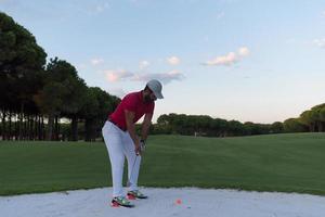 golfspeler raken een zand bunker schot Aan zonsondergang foto